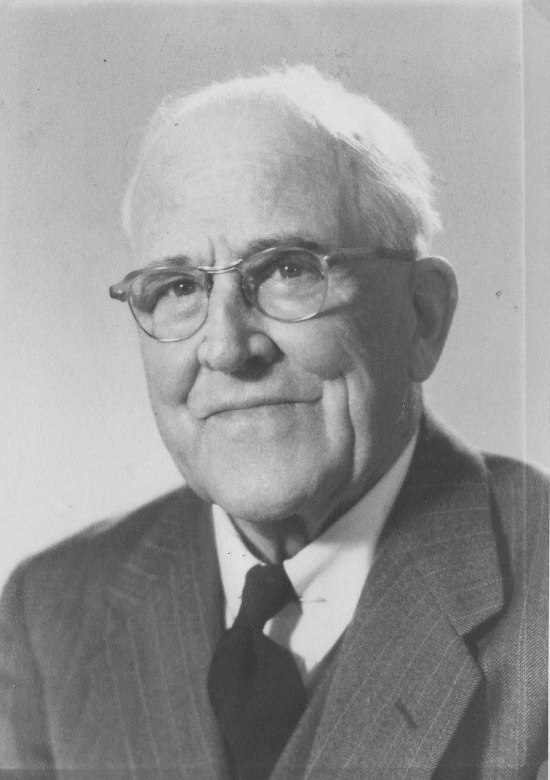Black and white portrait photograph of a middle-aged man wearing a suit and glasses